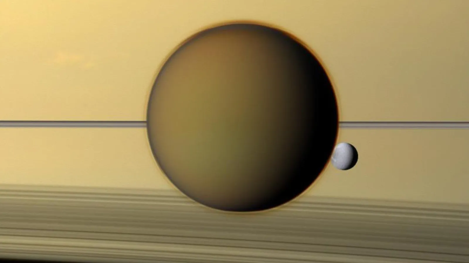 Titan nähtynä Saturnuksen pintaa vasten, mukana myös pienempi kuu Dione